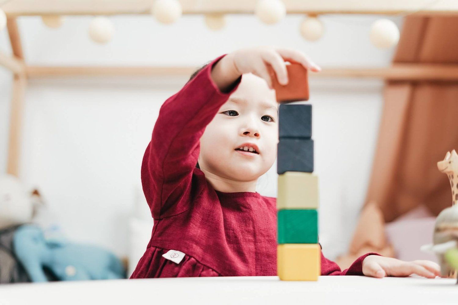 A young child stacking colourful wooden blocks on a table in a playroom.